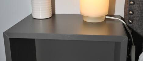 A modern bedside table with a white lamp, a small potted plant, and a white cylindrical object.