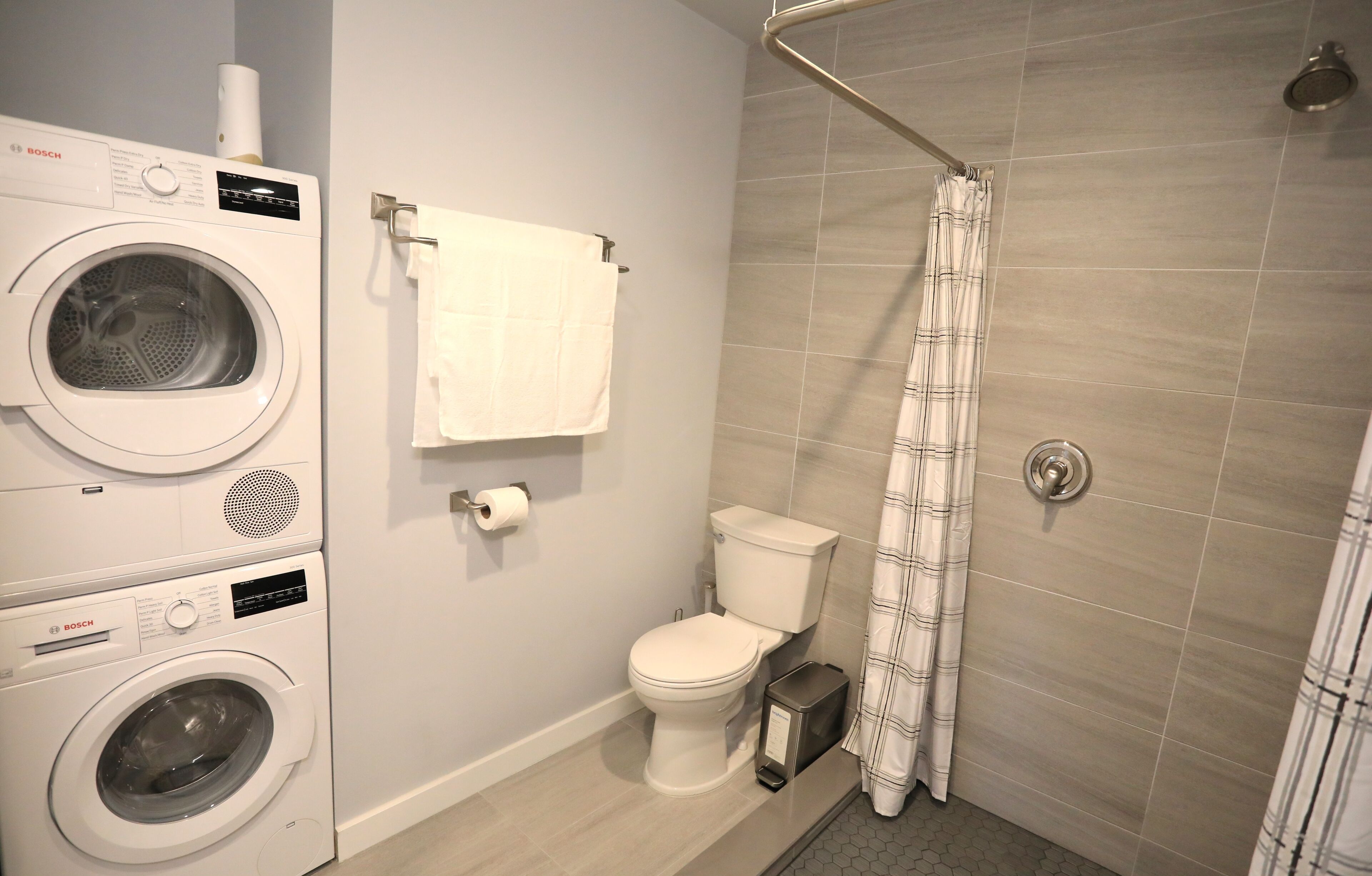 Un baño pequeño con lavadora Bosch, inodoro y ducha con cortina.
