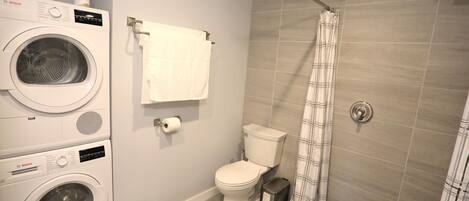Un baño pequeño con lavadora Bosch, inodoro y ducha con cortina.