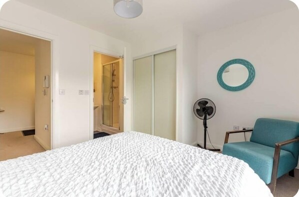 A bedroom with a large bed, a blue chair, a fan, and a mirror on the wall.