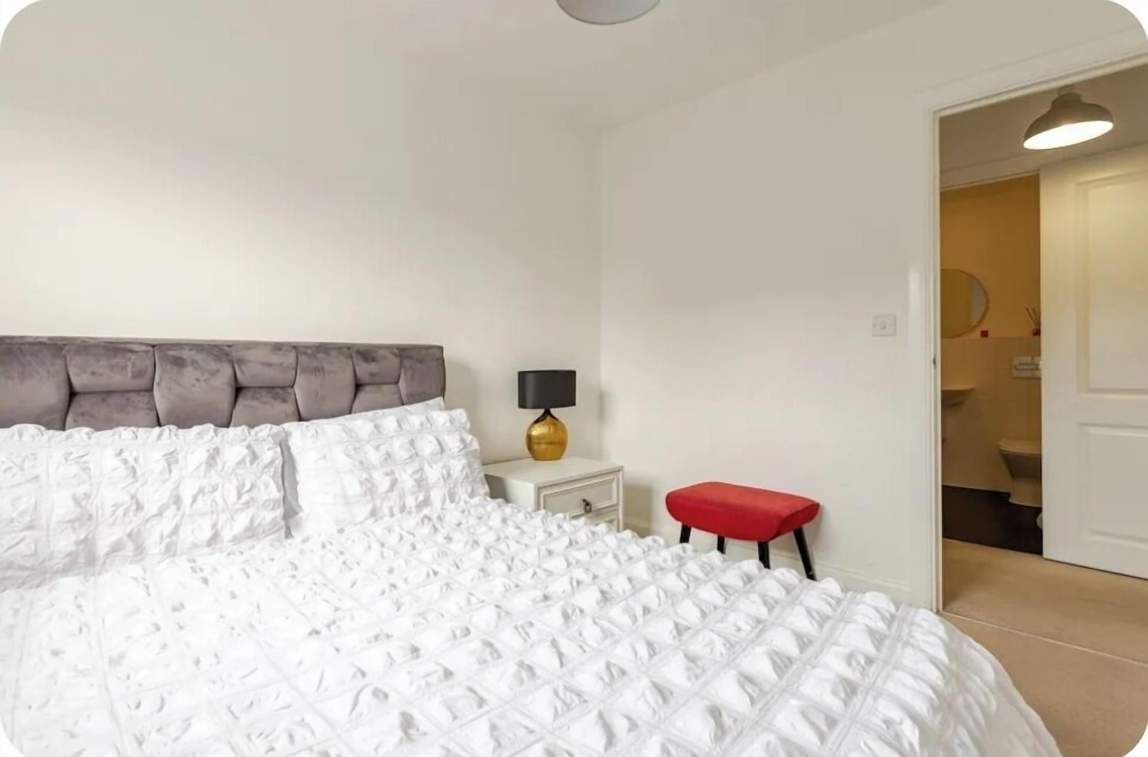 A bedroom with a large bed, a bedside table with a lamp, and a red bench.