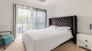 Une chambre à coucher avec un grand lit, une table de chevet, une chaise et une fenêtre avec des stores.
