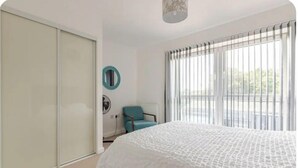 Une chambre avec un grand lit, une chaise, un radiateur et une fenêtre avec des stores.