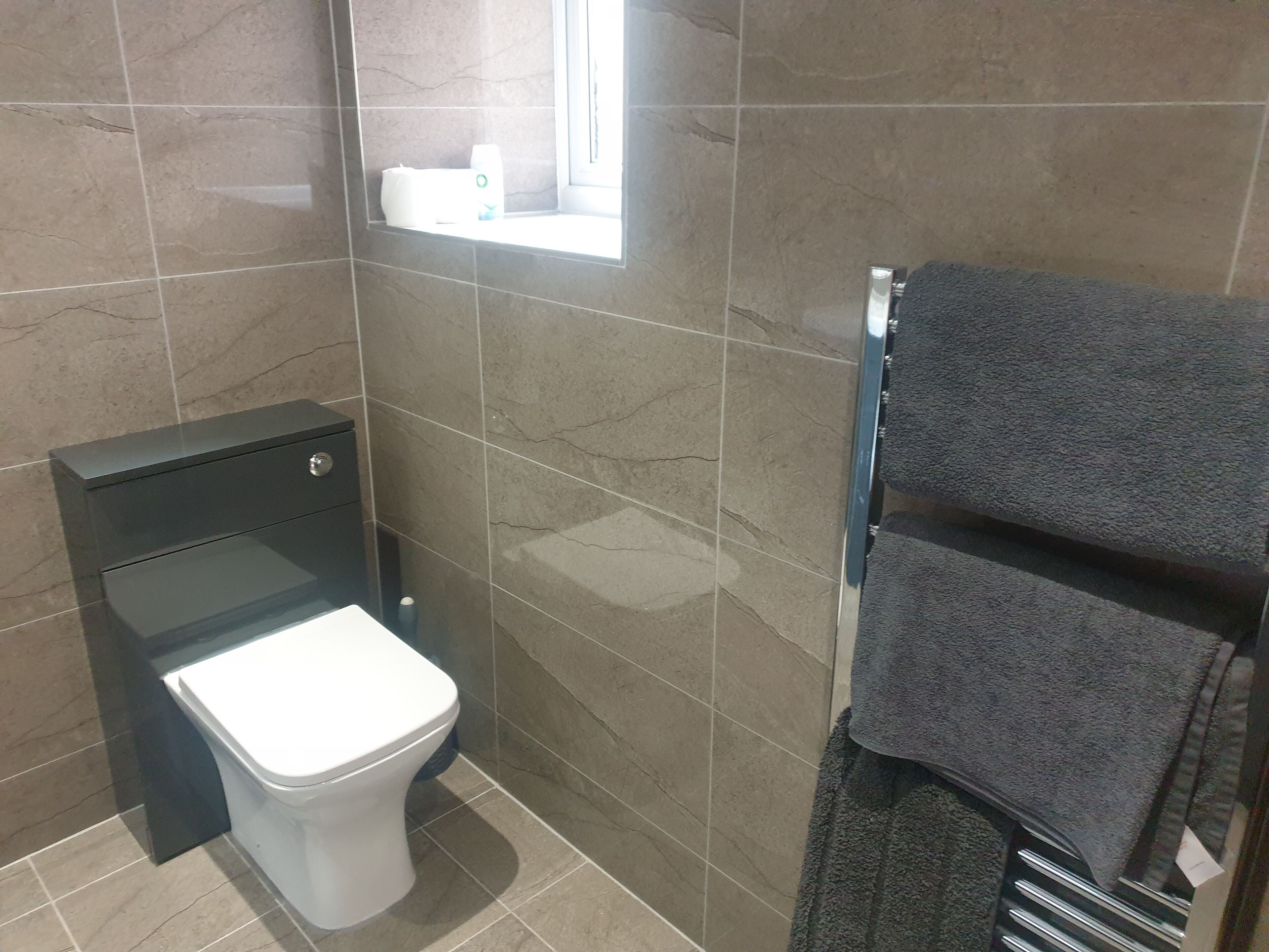 A bathroom with a toilet, a towel rack with a towel, and a shelf with toiletries.