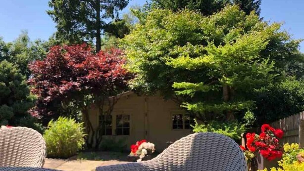 An outdoor patio with wicker furniture, a house in the background, and various trees and shrubs. - Cottage Hurst Green Sleeps 4, Views (Clitheroe)