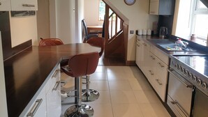 A modern kitchen with a central island, stainless steel appliances, and a dining area with two chairs. - Cottage Hurst Green Sleeps 4, Views (Clitheroe)