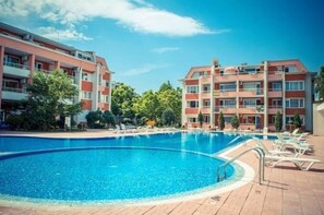 Piscina cercada por um terraço de tijolos, com um edifício de vários andares ao fundo.