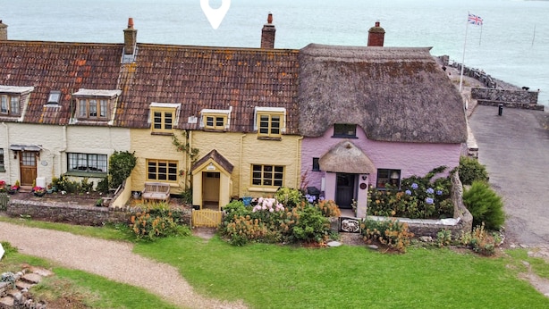 A coastal building with a thatched roof, a stone wall, and a flag.