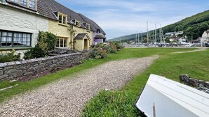 A coastal building with a thatched roof, stone walls, and a gravel path leading to a grassy area.