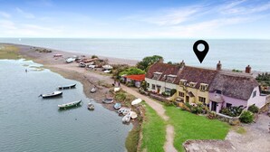 A coastal building with a thatched roof, surrounded by boats and a grassy area.