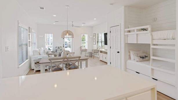 Un intérieur lumineux et blanc, avec un coin repas, des meubles blancs et un lit superposé agrémenté d’un coussin décoré avec le motif « endroit où je suis heureux/heureuse ».