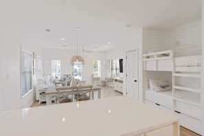 Un interior luminoso y blanco con comedor, muebles blancos y una cama litera con una almohada que dice 'lugar feliz'.
