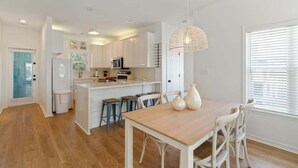 Une cuisine moderne avec des meubles blancs, un îlot central doté de tabourets et un luminaire suspendu.