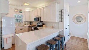 Une cuisine moderne avec des meubles blancs, un îlot central doté de tabourets, un réfrigérateur et un four à micro-ondes.