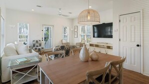 Un salon spacieux avec une table à manger en bois, des canapés blancs et un grand téléviseur fixé au mur.