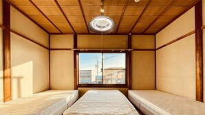 Ein Zimmer mit zwei Einzelbetten, einem Fenster mit Blick auf Gebäude und einer Holzbalkendecke.