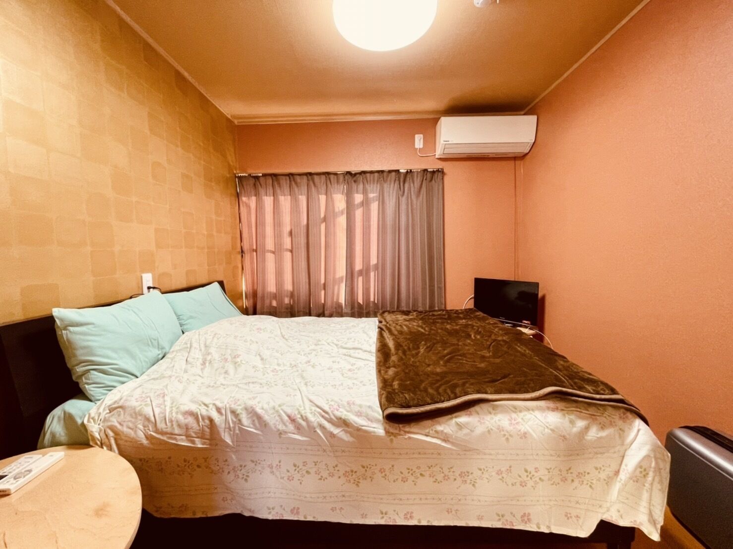 Um quarto pequeno e acolhedor, com uma cama, uma mesa redonda e um aparelho de ar condicionado na parede.