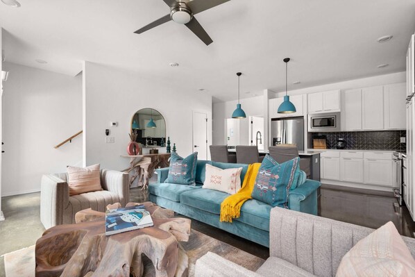 A modern living room with a blue sofa, wooden coffee table, and a dining area with a kitchen in the background. - Myrtle One ~ This is a combined listing made of two adjoining 4BR/4BA Condos with adjoining rooftops (Nashville)