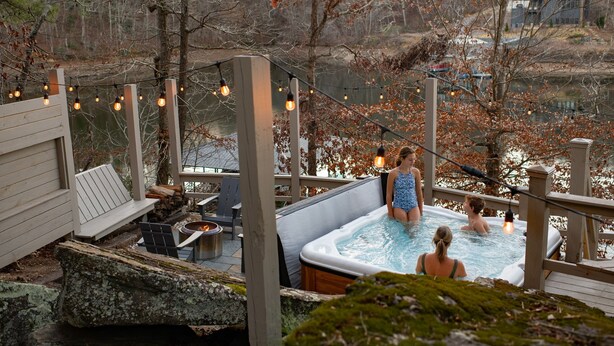 Ein Whirlpool auf einer Holzterrasse mit Lichterketten, mit Blick auf einen See.