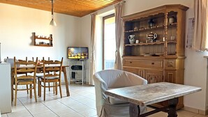 Zona pranzo con tavolo e sedie in legno, televisore su un supporto e mobiletto contenitore con ripiani.
