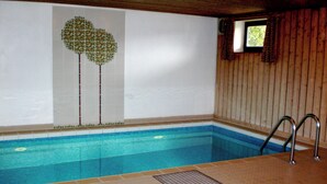 Una piscina interna con pavimento piastrellato, un coperchio per lo scarico e una parete in legno con una finestra.