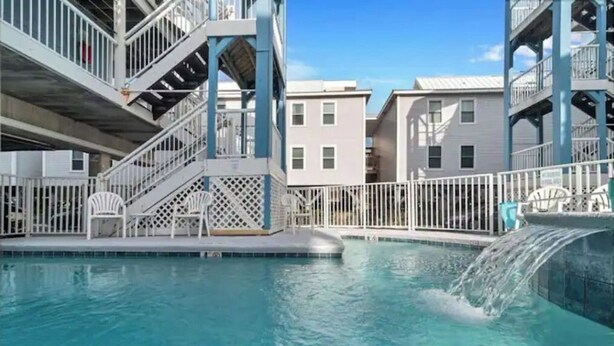 A swimming pool with a waterfall feature, surrounded by a white fence and a building with multiple balconies. - Sunchase Beachside Condo, Gulf Shores Updated Unit (Gulf Shores)