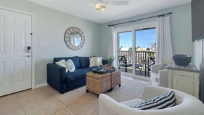 A living room with a blue sofa, a white armchair, a wicker coffee table, and a large mirror on the wall. - Sunchase Beachside Condo, Gulf Shores Updated Unit (Gulf Shores)