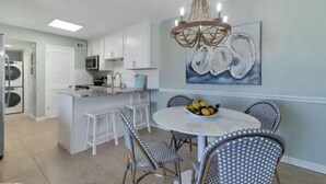 A modern kitchen with white cabinetry, a central island, and a dining area with a round table and chairs. - Sunchase Beachside Condo, Gulf Shores Updated Unit (Gulf Shores)