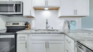 A modern kitchen with white cabinets, a stainless steel microwave, and a sink. - Sunchase Beachside Condo, Gulf Shores Updated Unit (Gulf Shores)