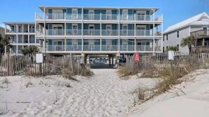 A multi-story beachfront hotel with balconies, a sandy beach in front, and a wooden fence. - Sunchase Beachside Condo, Gulf Shores Updated Unit (Gulf Shores)