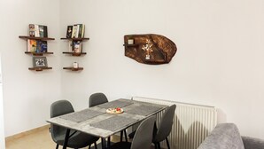 A dining area with a table set for four, surrounded by chairs. There are bookshelves above the table with various books and decorative items. A unique wooden wall art piece is mounted on the wall. - Kerkini Houses (Sintiki)