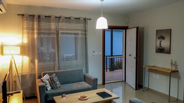 A living room with a sofa, a coffee table, a lamp, a balcony door, and a painting on the wall. - Kerkini Houses (Sintiki)