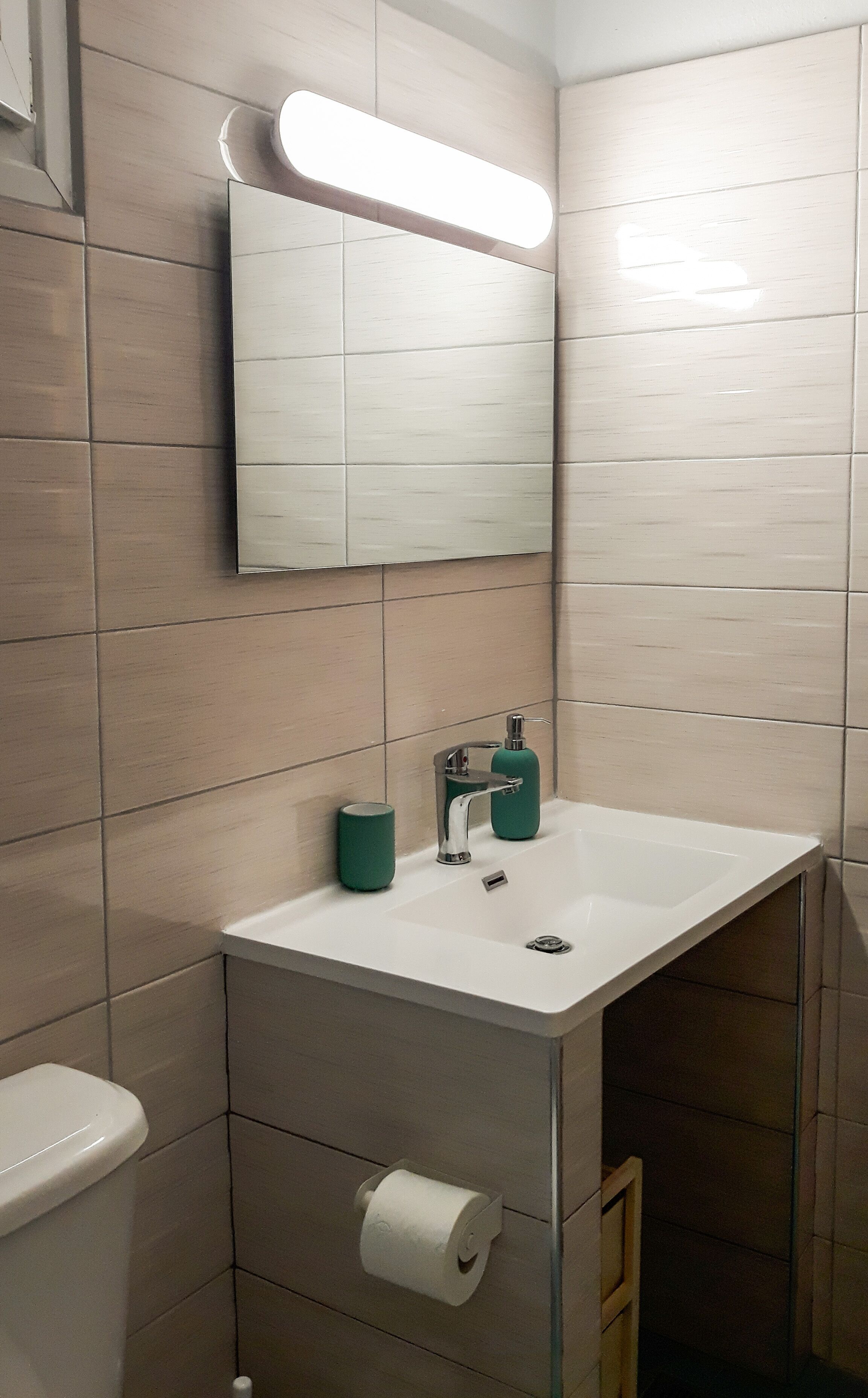 Een badkamer met een witte wastafel, een groene zeepdispenser en een toilet.