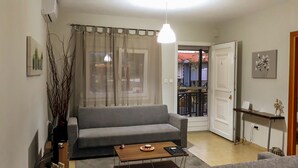 A living room with a grey sofa, a coffee table, a hanging light fixture, and a door leading to an outdoor balcony. - Kerkini Houses (Sintiki)