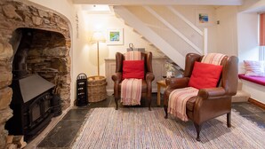 Una sala de estar acogedora con chimenea de piedra, sillones de cuero, un tapete estampado y una escalera que sube.