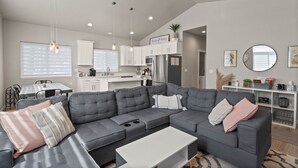 A modern living room with a grey sectional sofa, a white coffee table, and a dining area with a kitchen in the background. - PNW ~ Bayview Bigfoot steps to Lake Pend Oreille/Hot Tub (Bayview)