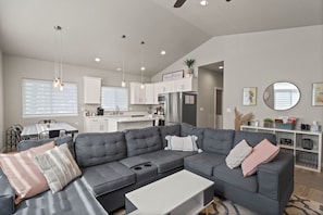 Een moderne woonkamer met een grijze modulaire bank, een witte salontafel, en een eethoek met een keuken op de achtergrond.