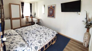 Ein Schlafzimmer mit Bett, Schreibtisch, Stuhl, Fernseher und einem dekorativen Wandbild.