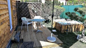 Eine Holzterrasse mit Tisch und Stühlen, einem Hängesessel und einem großen Sonnenschirm.