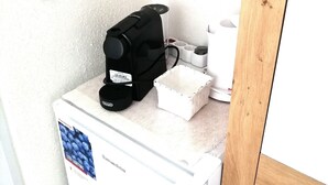 Eine kleine Küchenzeile mit einem weißen Kühlschrank, einer schwarzen Kaffeemaschine und einem weißen Kaffeekännchen auf der Arbeitsfläche.