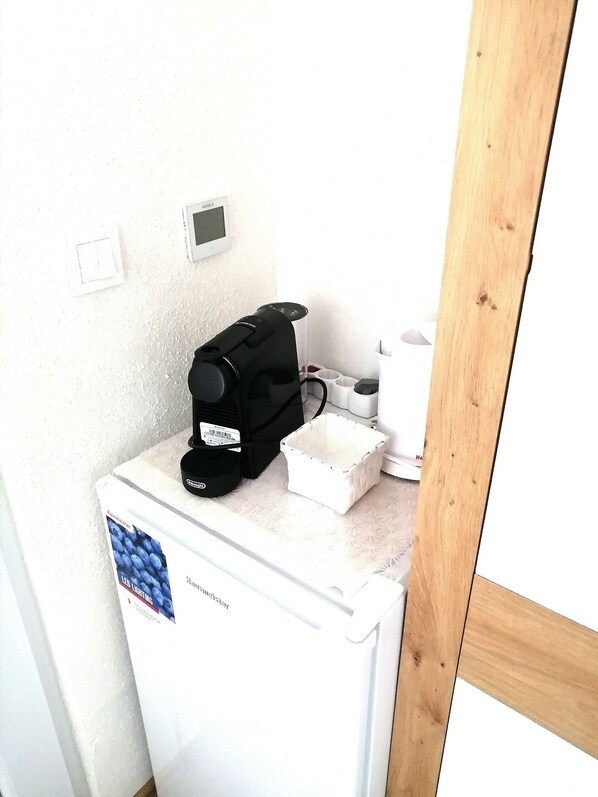 Una pequeña kitchenette con refrigerador, cafetera y una cesta blanca.