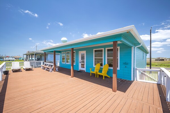 A blue building with a wooden deck, white railings, and yellow Adirondack chairs.