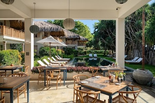 Uma área de refeições ao ar livre com estruturas de telhado de palha, cadeiras de lounge e uma piscina.