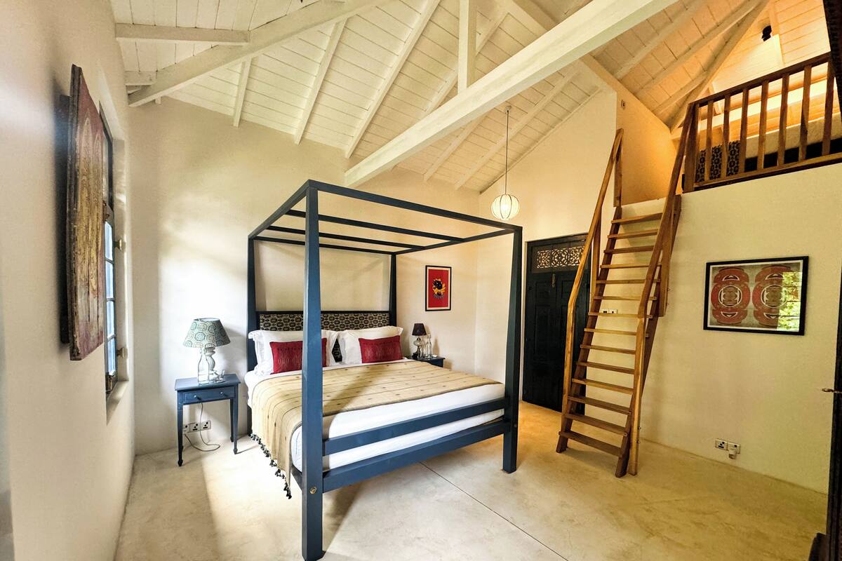 A four-poster bed with a wooden ladder, a nightstand with a lamp, and a framed picture on the wall.