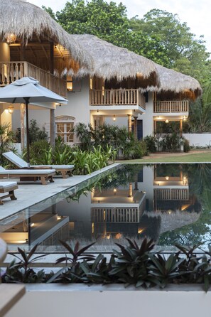 Un resort con piscina, edificios de techo de paja y abundante vegetación.
