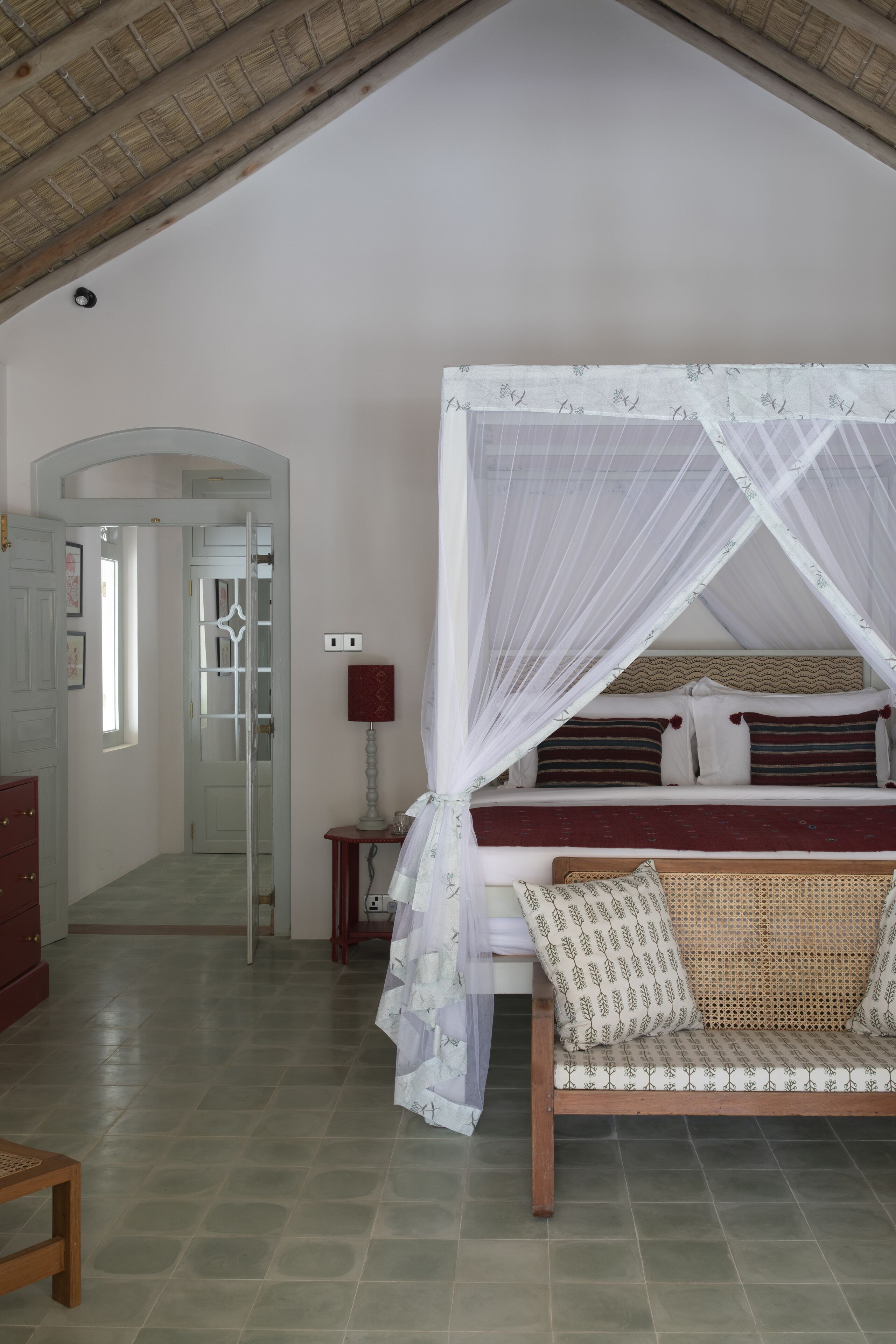 A bedroom with a canopy bed, a sofa, a small table, and a door leading to another room.