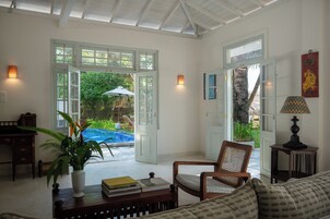 Um quarto espaçoso com uma grande porta aberta para uma área de piscina, uma cadeira de madeira, uma pequena mesa com livros e um abajur.