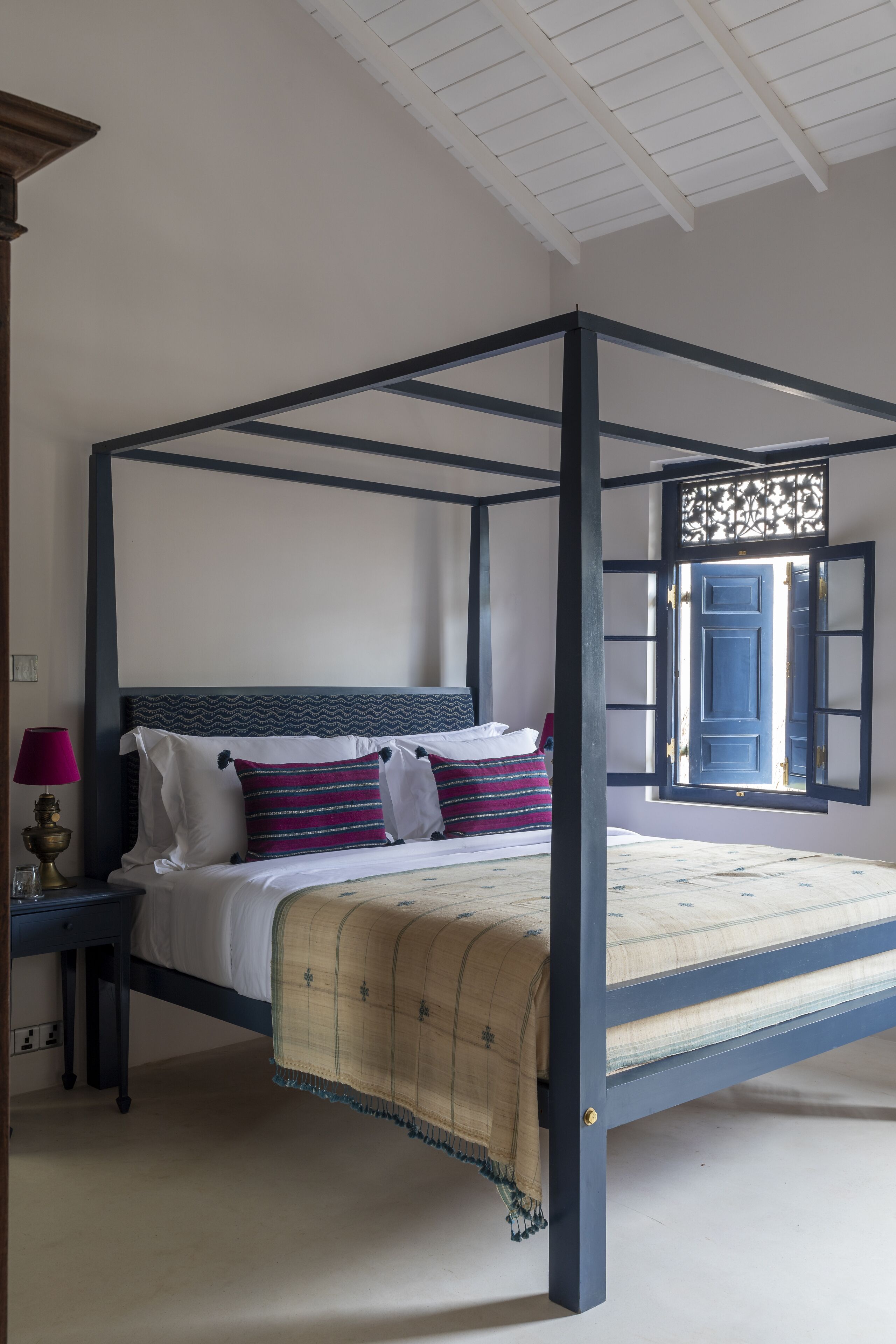 Ein Bett mit Baldachin, mit blauem Gestell, weißer Bettwäsche und einer beigen Decke.