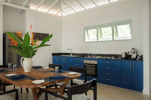 A modern kitchen with blue cabinets, a stainless steel refrigerator, and a dining area with a wooden table and chairs. - Halcyon Mawella (Morakatiyara)