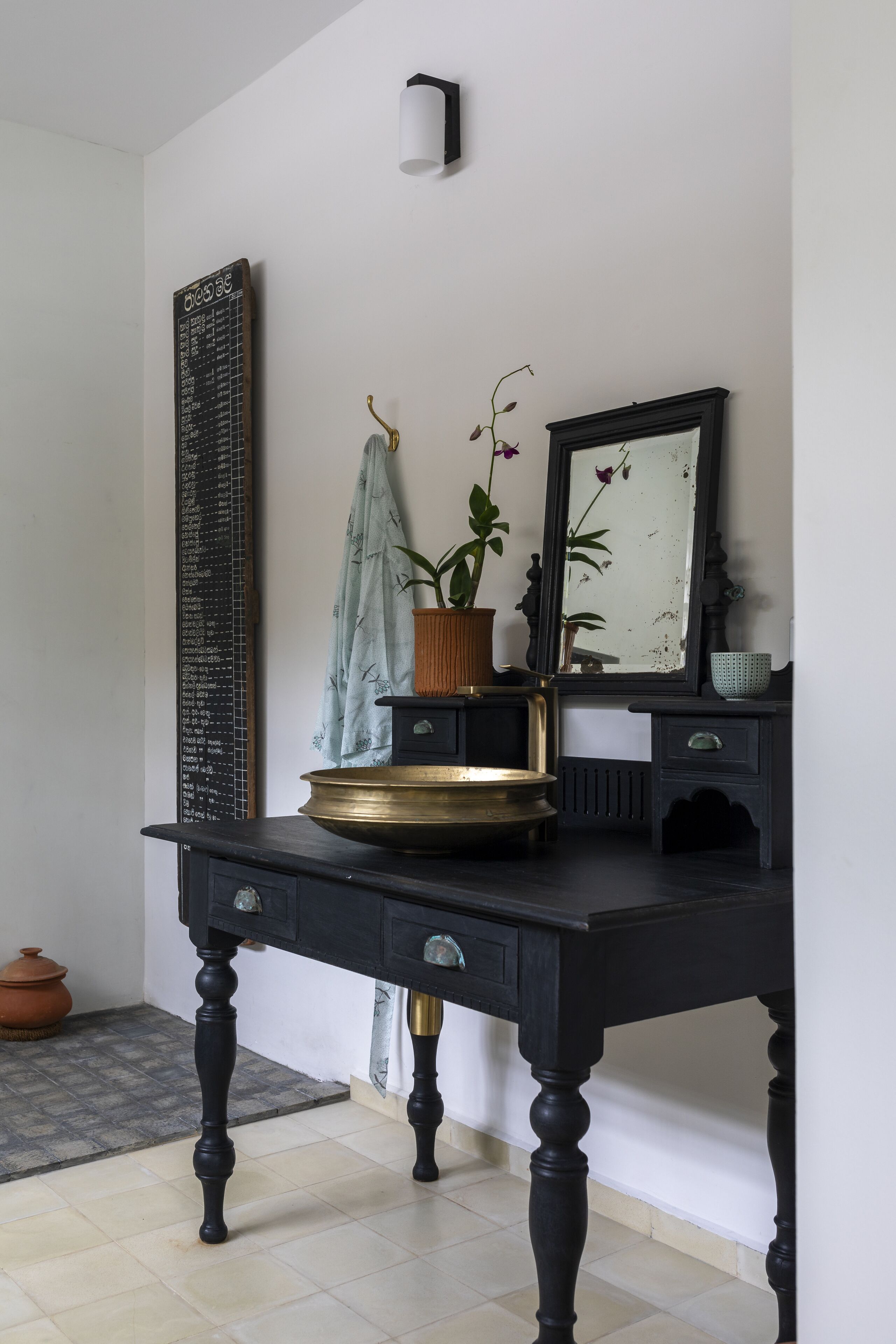 A black wooden desk with a brass tray, a potted plant, and a mirror.